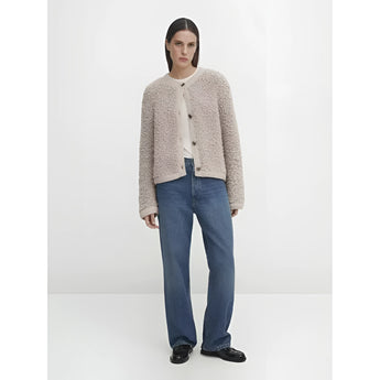 A woman wearing a navy bouclé jacket over a dress shirt, featuring a chunky knit texture. The jacket includes a collar, long sleeves, and resembles a blazer style, suitable for winter wear. The outfit is complemented by jeans, creating a casual yet polished look.