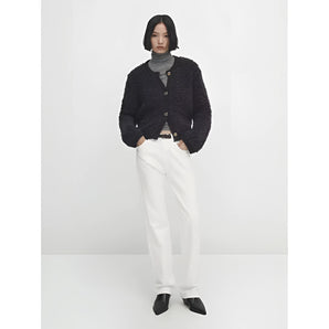 
A woman wearing a navy bouclé jacket, which is a chunky knit winter cardigan, styled over a dress shirt and jeans. The jacket features long sleeves and showcases an elegant, cozy design suitable for winter wear.