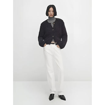 
A woman wearing a navy bouclé jacket, which is a chunky knit winter cardigan, styled over a dress shirt and jeans. The jacket features long sleeves and showcases an elegant, cozy design suitable for winter wear.