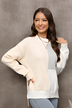 
A woman smiling while wearing a neutral tone color-block sweater, showcasing trendy fall knitwear with distinct sections of color. The sweater features a comfortable fit with attention to fashion design, including long sleeves and a stylish collar.