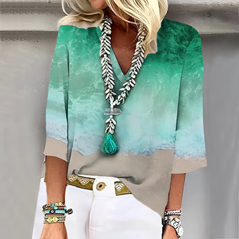 Woman wearing a green V-neck blouse with a beach scene design, paired with a tassel necklace, in size 3XL.