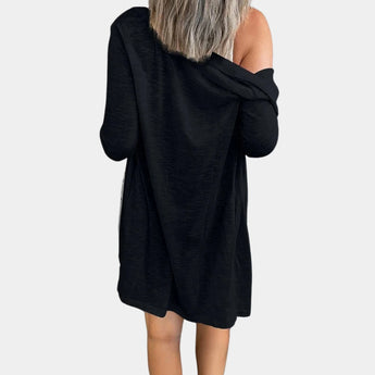 
A woman wearing an off-shoulder black mini dress with long sleeves and pockets, showcasing a casual yet stylish look. The dress accentuates the shoulders and waist, providing a chic appearance.