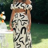 Off-shoulder black and white two-piece dress worn by a woman with a stylish hairstyle, smiling outdoors amidst greenery, perfect for a summer garden party.