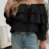 
Woman wearing an off-shoulder ruffle blue blouse with a bow-tie front, styled with her hair pulled back, showcasing the blouse's elegant neckline and flowing textile.
