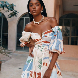 
Boho chic off-shoulder tribal mini dress with pom-pom trim, featuring a relaxed fit and short sleeves, styled on a woman with black hair.