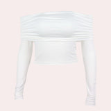 
A woman wearing an off-shoulder white long sleeve crop top, styled with light grey casual shorts. The top features a fitted design accentuating the waist and elbows, perfect for stylish fall fashion.
