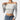 A woman wearing an off-shoulder white long sleeve crop top, showcasing a stylish fall fashion look. The top fits snugly around the waist, accentuating her shoulders and arms.
