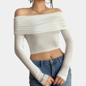 
A woman wearing an off-shoulder white long sleeve crop top paired with high-waisted jeans, showcasing a stylish fall fashion look. The top accentuates her shoulders and arms, creating an elegant and trendy appearance.