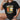 A black Oktoberfest Cartoon Tee featuring a humorous design of "Frank & Stein" characters, suitable for beer festival enthusiasts. The shirt displays detailed imagery and text with a playful font, styled with short sleeves and a casual fit, available in size XL.