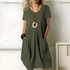 Olive green casual midi dress featuring short sleeves, side pockets, and a comfortable fit, displayed on a mannequin in a well-lit setting. The dress has a simple design with a round neckline and falls to a midi length, perfect for everyday wear.