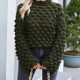
A woman wearing an olive green chunky knit pullover with puff sleeves, styled as fall fashion. She is accessorized with eyewear and has a fashionable hairstyle. The pullover features a cozy design, ideal for outerwear, and is paired with black leggings.