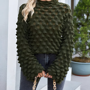 
A woman wearing an olive green chunky knit pullover with puff sleeves, styled as fall fashion. She is accessorized with eyewear and has a fashionable hairstyle. The pullover features a cozy design, ideal for outerwear, and is paired with black leggings.