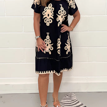 A woman wearing an olive green floral bohemian dress, suitable for casual chic summer festivals, styled with loose flowing fabric and a relaxed fit. The dress is a one-piece garment with a day dress design, highlighting elements like shoulders and arms. The model's hair is styled casually, and she is wearing shoes. The color variant displayed is Nero in size 5XL.