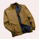 Olive green men's lightweight bomber jacket with zippered pocket, featuring a sleek design, ribbed collar and sleeves, and a full zipper closure. The jacket is displayed in a bronze color and size 2XL.