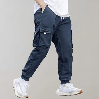 Olive green men's tapered cargo pants, showcasing a lightweight and fashionable utility design, with visible pockets and seams. A person models the pants, highlighting their fit around the thighs and knees.