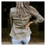 
A woman wearing an olive green slim fit utility jacket, styled with casual denim jeans, standing outdoors. The jacket features a collar and long sleeves, complementing her fall fashion look. She is accessorized with sunglasses and is surrounded by greenery.
