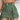 Olive green women's utility mini cargo skirt with a belt and pockets, displayed on a person wearing a white top.