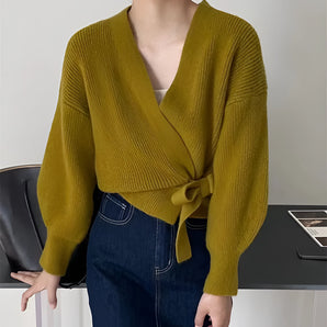 
A woman wearing an olive green V-neck wrap sweater paired with jeans, showcasing a casual yet chic autumn fashion look. The sweater features a draped neckline and long sleeves, emphasizing a relaxed and stylish fit.