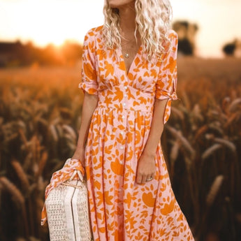 Orange floral V-neck maxi dress in boho chic style, worn by a smiling woman in nature during a summer photoshoot, featuring sleeves and a flowing one-piece design in size XL.
