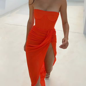 Orange strapless high slit ruched bodycon evening dress displayed on a mannequin, showcasing a form-fitting silhouette with a slit revealing the leg.