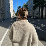 Oversized beige chunky knit turtleneck sweater worn by a person standing on a sidewalk outside during the daytime.