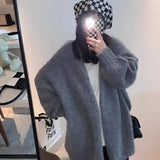 
A woman wearing an oversized gray chunky knit cardigan with long sleeves, featuring a cozy and casual winter fashion style. The cardigan is layered over a formal outfit, including a blazer and an overcoat, suitable for cold weather.