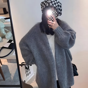 
A woman wearing an oversized gray chunky knit cardigan with long sleeves, featuring a cozy and casual winter fashion style. The cardigan is layered over a formal outfit, including a blazer and an overcoat, suitable for cold weather.