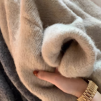 Oversized beige chunky knit women's cardigan draped on a model, highlighting the cozy texture perfect for winter fashion. The focus is on the soft, thick knit pattern and the relaxed fit of the cardigan, with subtle details like the model's hand and wrist adorned with minimal jewelry visible.