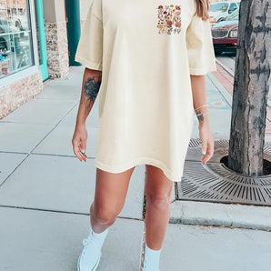 Oversized beige T-shirt dress with floral embroidery, featuring short sleeves, a round neckline, and reaching down to the thighs.