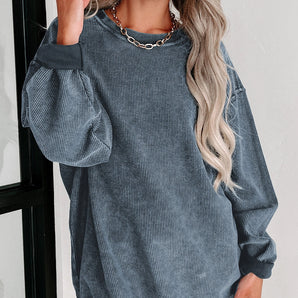Oversized blue corduroy pullover women's long sleeve sweater worn by a smiling woman with long hair, showcasing the shoulder and arm details against a white background.