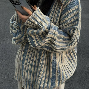 Oversized blue stripe knit sweater featuring long sleeves, shown on a woman wearing sunglasses and holding a mobile phone, capturing a casual autumn fashion style.