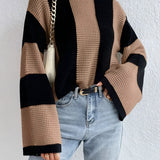 Oversized chunky black and tan striped knit sweater featuring long sleeves, perfect for autumn fashion. The sweater is modeled with jeans, showcasing a cozy and stylish look suitable for cooler weather.