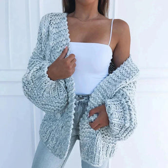 Oversized chunky blush pink cardigan worn by a woman, showcasing the cozy and relaxed fit with long sleeves and extended waist length. The cardigan displays a soft and warm textile, perfectly suited for winter fashion.