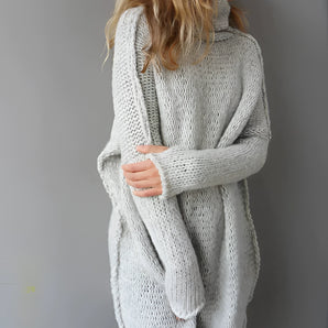 Woman wearing an oversized chunky knit sweater with a cozy turtleneck, showcasing winter fashion. She is standing with her hand on her hip, highlighting the sweater's long sleeves and textured fabric.