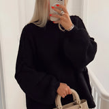 Oversized black knit sweater featuring long sleeves and a relaxed fit, ideal for elegant autumn fashion. The sweater has a wide neckline and is shown on a person with visible shoulder and waist details.
