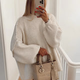 
A person wearing an oversized cream knit sweater with long sleeves, showcasing its elegant autumn fashion style. The sweater covers the shoulders and neck, paired with sunglasses and a white dress shirt underneath.