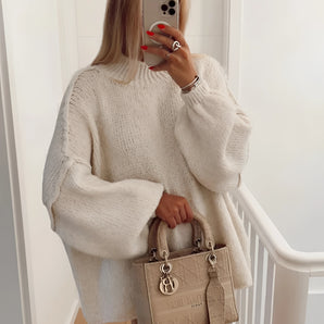 
A person wearing an oversized cream knit sweater with long sleeves, showcasing its elegant autumn fashion style. The sweater covers the shoulders and neck, paired with sunglasses and a white dress shirt underneath.