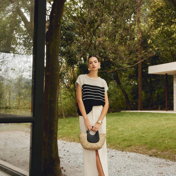 Oversized designer straw tote with a black handle, worn by a person standing in a natural setting, showcasing eco-friendly fashion.