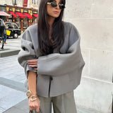 Oversized gray blazer with a cropped top and matching trousers, modeled by a person wearing sunglasses and holding a stylish bag, embodying a chic streetwear look.
