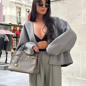 Oversized gray blazer paired with a cropped top and trousers, modeled by a person wearing sunglasses, showcasing a chic streetwear style.