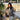 Oversized gray blazer paired with a cropped top and trousers, worn by a seated model. The outfit exudes chic streetwear style, complemented by fashionable eyewear. The setting includes a minimalist backdrop with a touch of greenery.