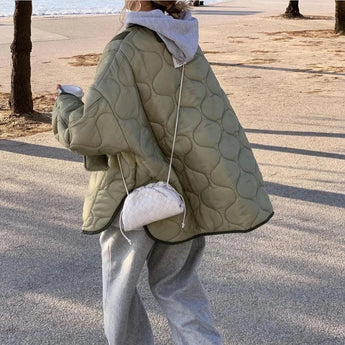 A woman wearing an oversized green quilted puffer jacket with long sleeves, standing outdoors, accessorized with sunglasses and casual autumn attire.