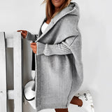 
A woman standing and wearing an oversized grey hoodie dress made from cozy knit material, featuring long sleeves and pockets.