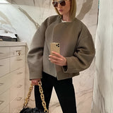 Oversized grey sweater paired with a gold chain bag, worn by a woman with sunglasses, standing in front of white cabinetry.
