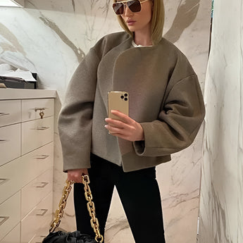 Oversized grey sweater paired with a gold chain bag, worn by a woman with sunglasses, standing in front of white cabinetry.