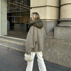 Oversized khaki hooded jacket for women, featuring a minimalist urban fashion style, with knee-length design and long sleeves, displayed on a grey sidewalk background.
