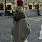Oversized khaki hooded jacket worn by a woman standing outdoors, showcasing minimalist urban fashion with long sleeves and a trench coat style.