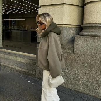 Oversized khaki hooded jacket worn by a woman standing on a road surface, showcasing minimalist urban fashion with the jacket reaching thigh-length and featuring long sleeves.