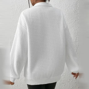 
A woman wearing an oversized white textured knit sweater, featuring long sleeves and a cozy, loose fit, perfect for winter fashion. The sweater is styled with emphasis on comfort and warmth.
