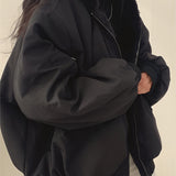 Oversized women's black bomber puffer jacket featuring a trendy winter fashion design with visible sleeves and a high collar. A hand is adjusting the collar, highlighting the jacket's warm, protective features.